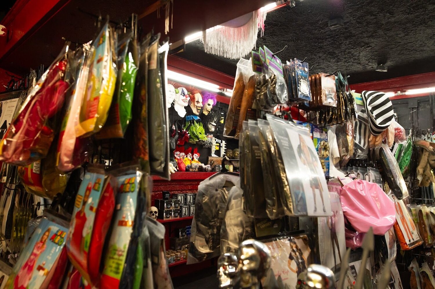 Inside Whips 'n Furs: walls packed with bagged costumes, clown and monster masks, and a dragon mask under red lighting